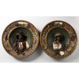 A pair of Continental moulded pottery chargers depicting busts of pirate and female figure
