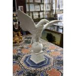 A large white glazed pottery model of an eagle standing wings outswept on an orb