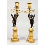 A SUPERB PAIR OF FRENCH EMPIRE BRONZE AND ORMOLU CANDLESTICKS as a pair of winged cupids holding