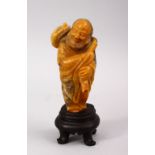 A GOOD QUALITY NATURAL COLOUR CHINESE CARVED SOAPSTONE FIGURE OF ROHAN, stood holding a staff over