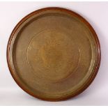 A LARGE ISLAMIC BRASS CIRCULAR TRAY WITH HARDWOOD MOUNT, WITH KUFIC CALLIGRAPHY, 77cm.