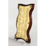 AN EARLY 20TH CENTURY BRASS AND OAK CRIBBAGE BOARD, of serpentine outline. 11ins x 5.5ins.