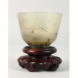 A GOOD JADE CUP on a wooden stand. 2.5ins diameter.