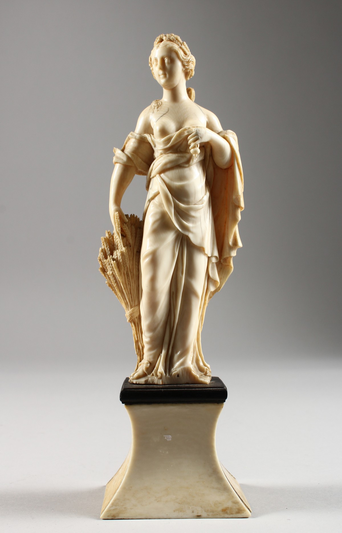 AN 18TH CENTURY CARVED IVORY FIGURE OF A YOUNG FEMALE FIGURE depicting AUTUMN, standing on a plinth.