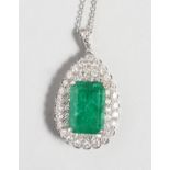 A GOOD 18CT WHITE GOLD PEAR SHAPED PENDANT inset with a central rectangular emerald, surrounded by