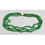 A THREE ROW STRING OF JADE BEADS, with an 18ct gold and cabochon coral clasp. 20ins long.