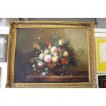 A large and impressive still life of flowers in an urn on a ledge, in a decorative gilt frame.