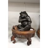 A Japanese style cast metal model of a monkey seated on a hardwood stand.