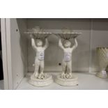 A pair of continental white porcelain candlesticks modelled as cherubs holding aloft a shell.