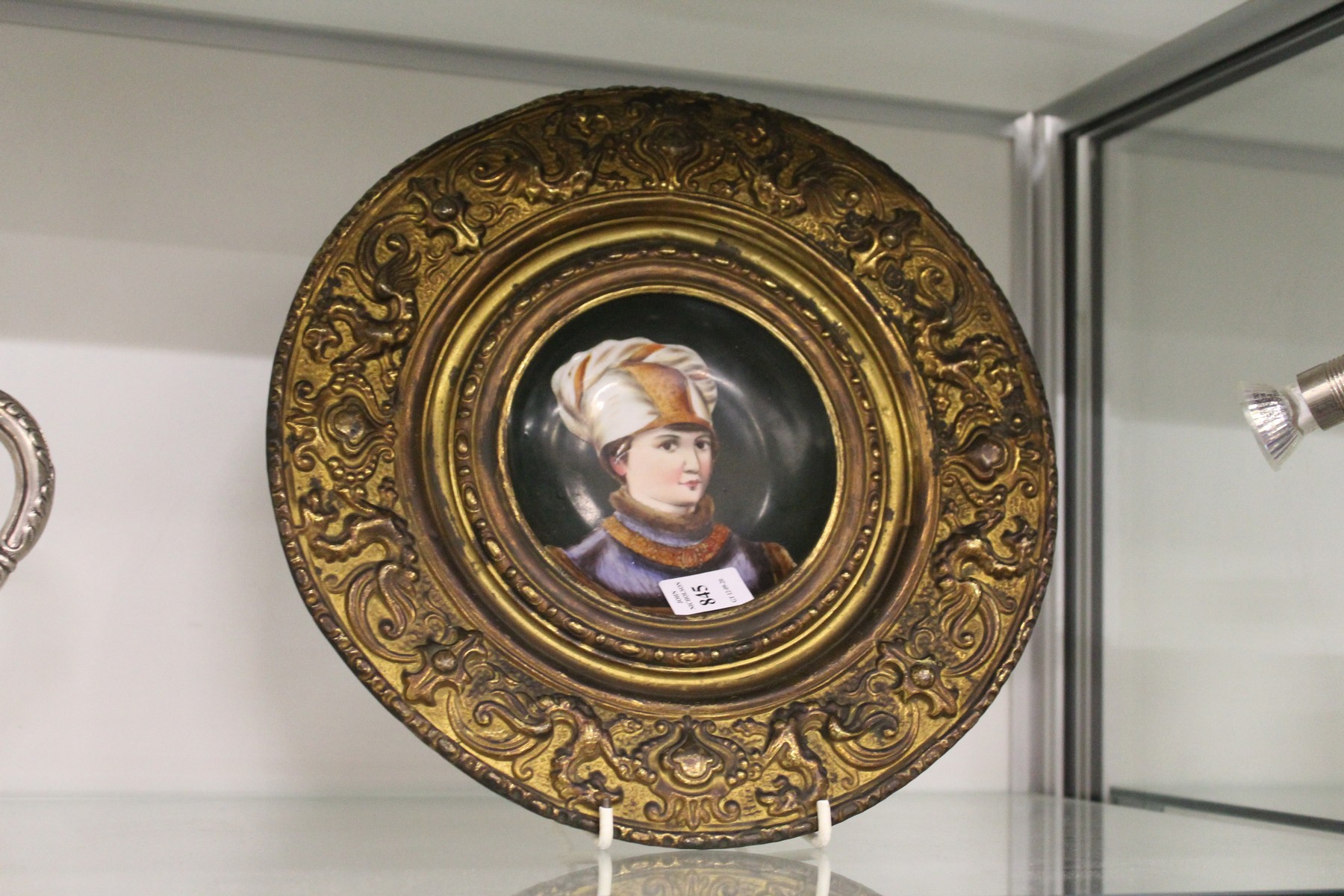 A continental circular porcelain portrait plaque in an embossed brass frame.