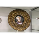 A continental circular porcelain portrait plaque in an embossed brass frame.