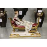 A continental porcelain model of a young lady reclining on a day bed.