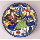 A PERSIAN QAJAR GLAZED POTTERY DISH of two figures seated, 24cm