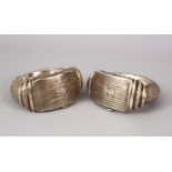 A GOOD PAIR OF ISLAMIC SILVER COATED LOCKING BANGLES, each carved decoration of hanging motifs, 11cm