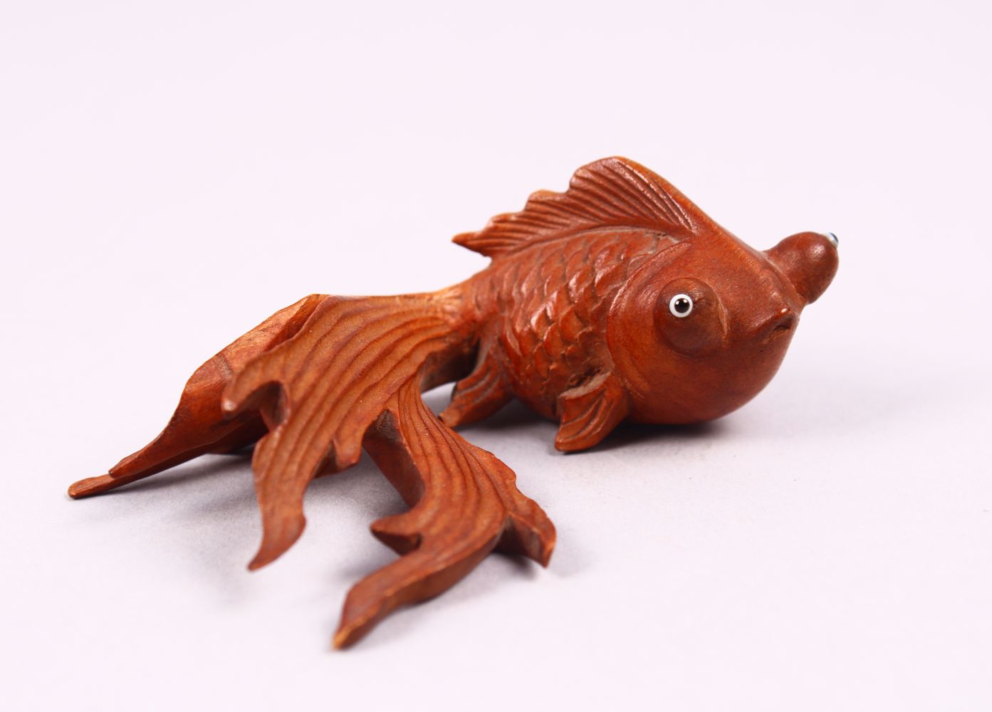 A CHINESE CARVED BOXWOOD/ WOODEN FIGURE OF A GOLDFISH, with glass inset eyes, 3cm x 8cm.