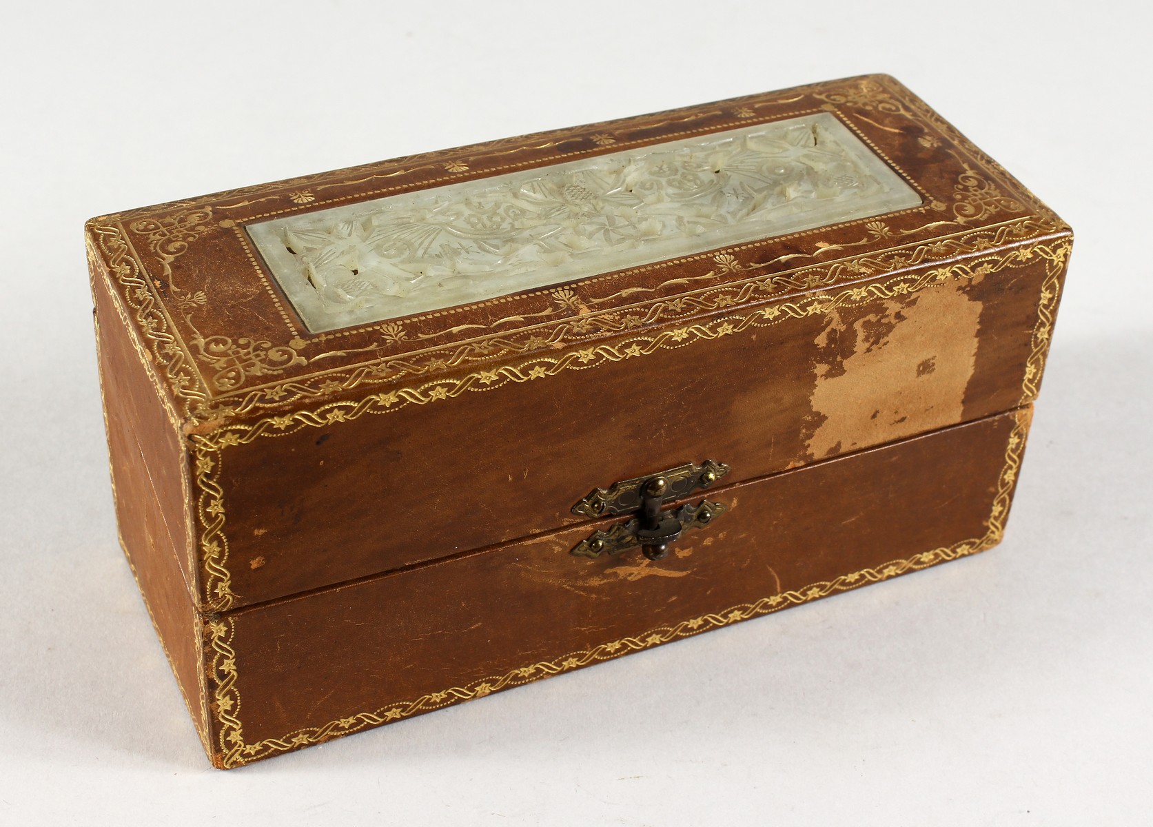 A GILT TOOLED LEATHER BOX INSET WITH A PIERCED JADE PANEL. 7ins long.