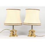 A GOOD PAIR OF ORMOLU TABLE LAMPS, the concave sided base with three kneeling figures. 13ins high.