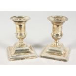 A SMALL PAIR OF SILVER CANDLESTICKS on square bases. 4ins high. Sheffield 1902.