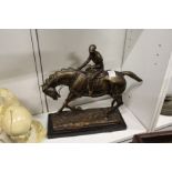 A bronze group of a jockey on horseback on a marble base.