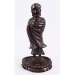 A 19TH CENTURY CHINESE CARVED HARDWOOD FIGURE OF A LUOHAN, stood wrapped in his gowns, upon a carved