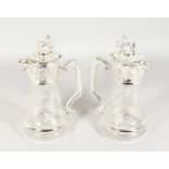 A PAIR OF ETCHED GLASS CLARET JUGS WITH PLATED MOUNTS AND LION FINIALS. 10.75ins high.