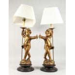 A GOOD PAIR OF ITALIAN CARVED WOOD AND GILDED CHERUB LAMPS AND SHADES on circular bases. 27ins