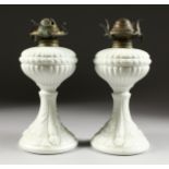 A PAIR OF WHITE OPALINE OIL LAMPS with dolphin supports on circular bases. 9ins high.