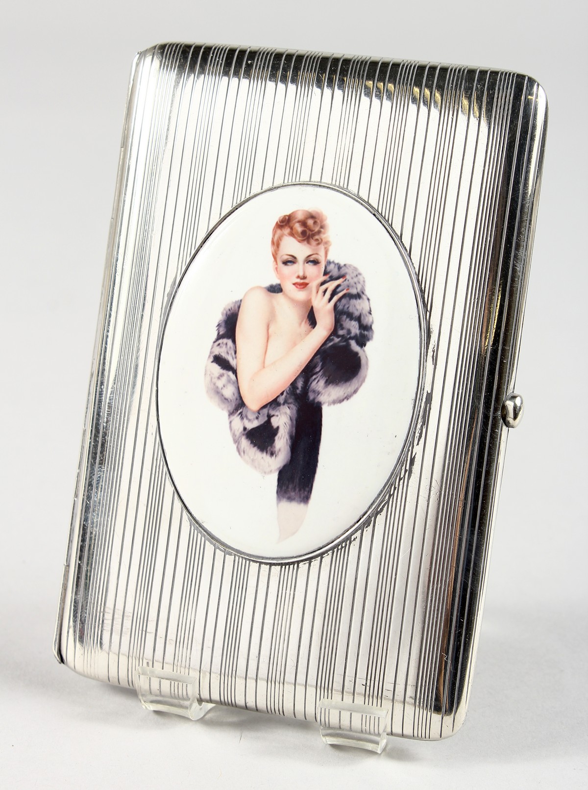 AN ENGINE TURNED SILVER CIGARETTE CASE, with an oval of a model with a fur coat.