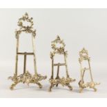 A SET OF THREE BRASS EASELS. 16ins, 11ins and 9ins high.