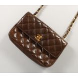 A GOOD CHANEL BROWN LEATHER PADDED PURSE with leather and gilt long handle. 7ins long, in a black