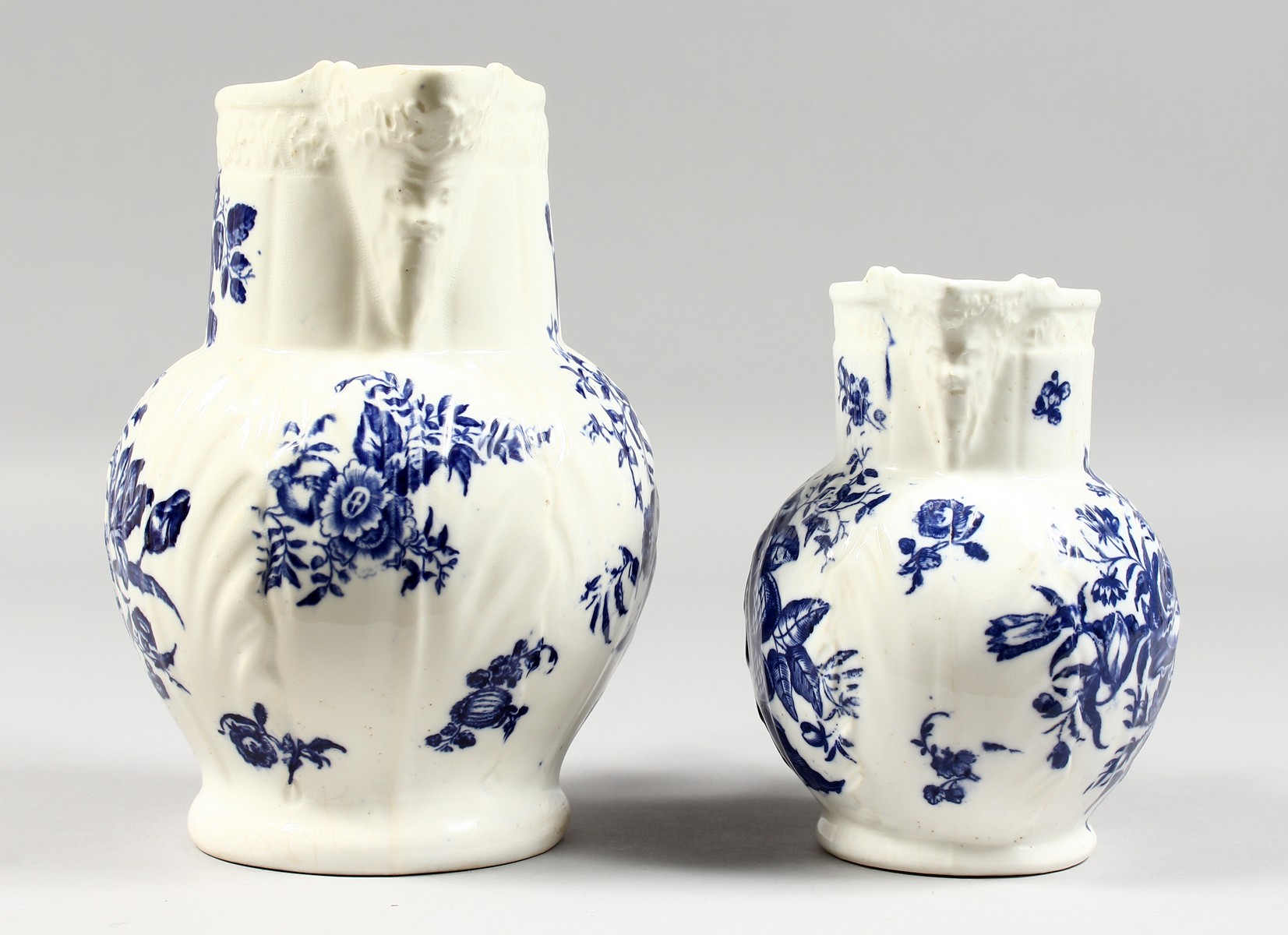 A GRADUATED PAIR OF DECORATIVE ENGLISH PORCELAIN MASK JUGS printed with fir cones and roses in