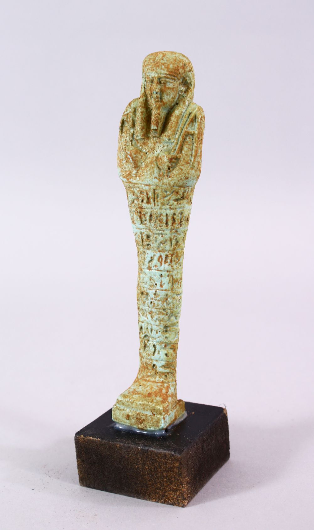 A CARVED POTTERY EGYPTIAN SHABTI, stoof upon a wooden base, 19cm high.