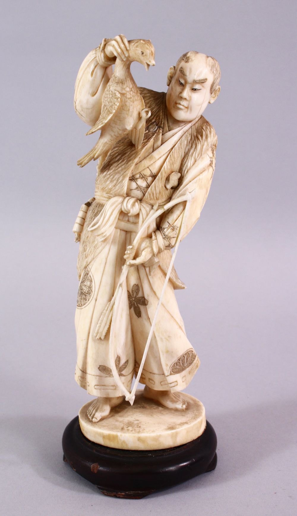 A FINE JAPANESE MEIJI PERIOD CARVED IVORY OKIMONO OF A HUNTSMAN, stood holding his catch with his