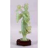 A CHINESE CARVED JADE FIGURE OF GUANYIN, stood holding a bouquet above her head, on a wooden