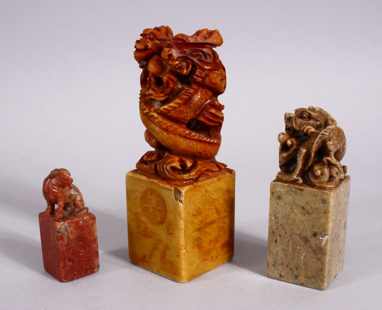 THREE CHINESE CARVED SOAPSTONE SEALS, each carved with dragons and lion dogs, two bases carved