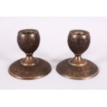 A GOOD PAIR OF ISLAMIC QAJAR WHITE METAL CANDLESTICKS, carved with figures in fez, 9cm diameter x