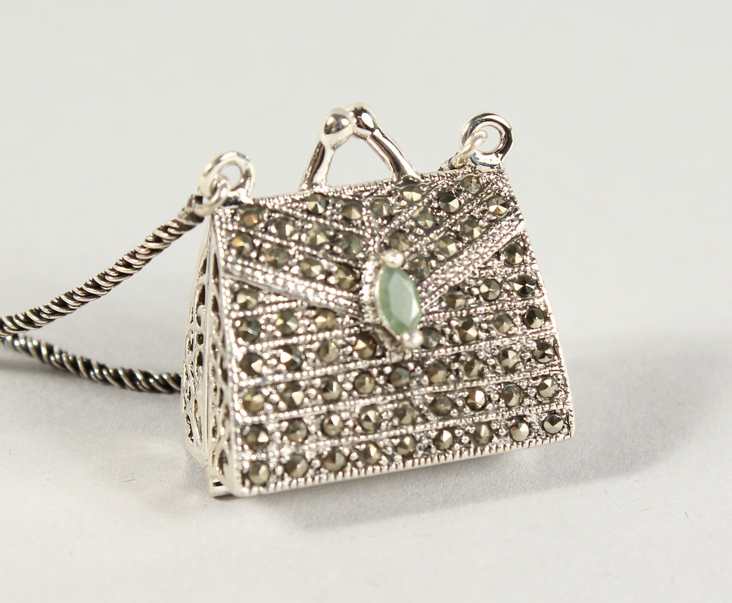 A SILVER, MARCASITE AND EMERALD SET HANDBAG PENDANT on a chain.