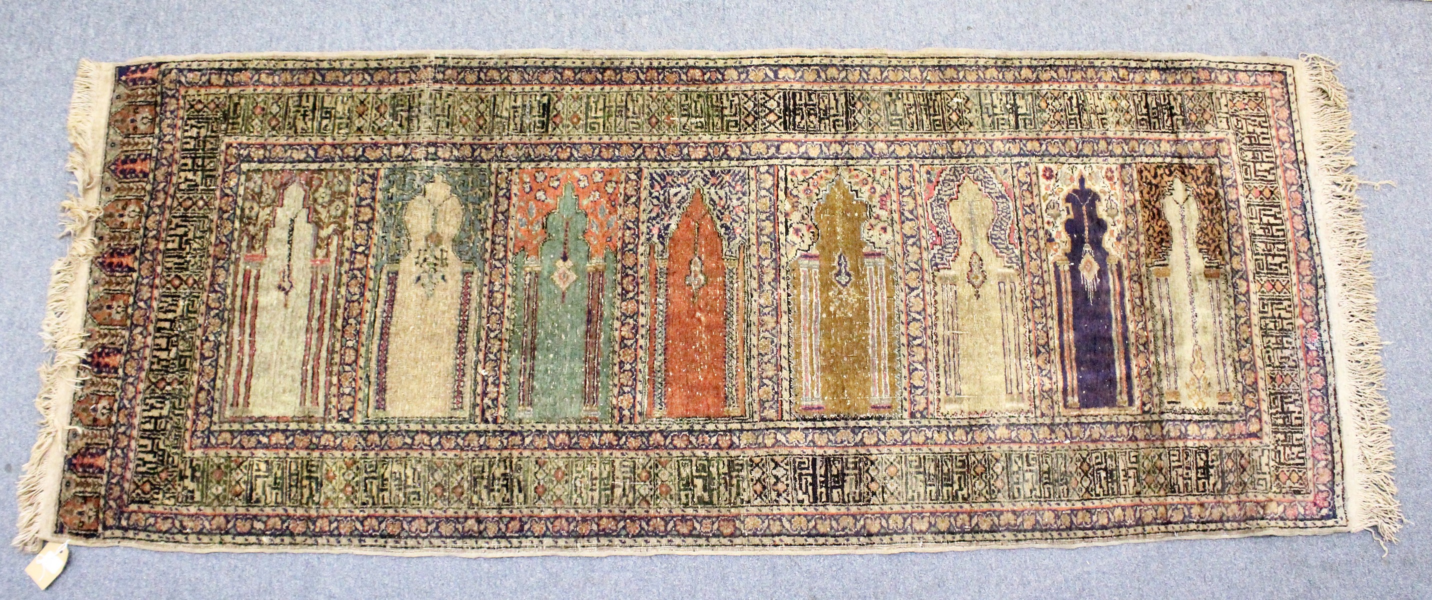 AN UNUSUAL PERSIAN PRAYER RUG, the central panel with eight arches and hanging lamps, within a