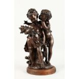 A BRONZE GROUP, depicting a young boy whispering to a young girl, on a wooden base. 17ins high.