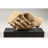 A POTTERY SCULPTURE OF CLASPED HANDS, on a marble base. 9ins long.