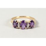 A 9CT GOLD THREE STONE OVAL AMETHYST AND DIAMOND RING.