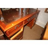 A polished as yew double pedestal desk with brown tooled leather lined top, fitted nine drawers,