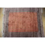 A cotton pile rug of traditional design on an orange ground and multi-bordered in shades of fawn,