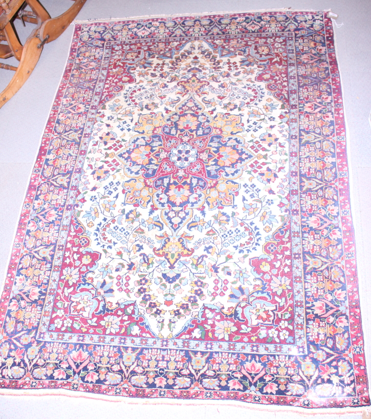 A Persian rug with central medallion and flower decoration in shades of red, blue, green and