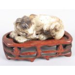 A Chinese carved jade figure of a resting dog, 3 1/4" wide, and an unmatched hardwood stand