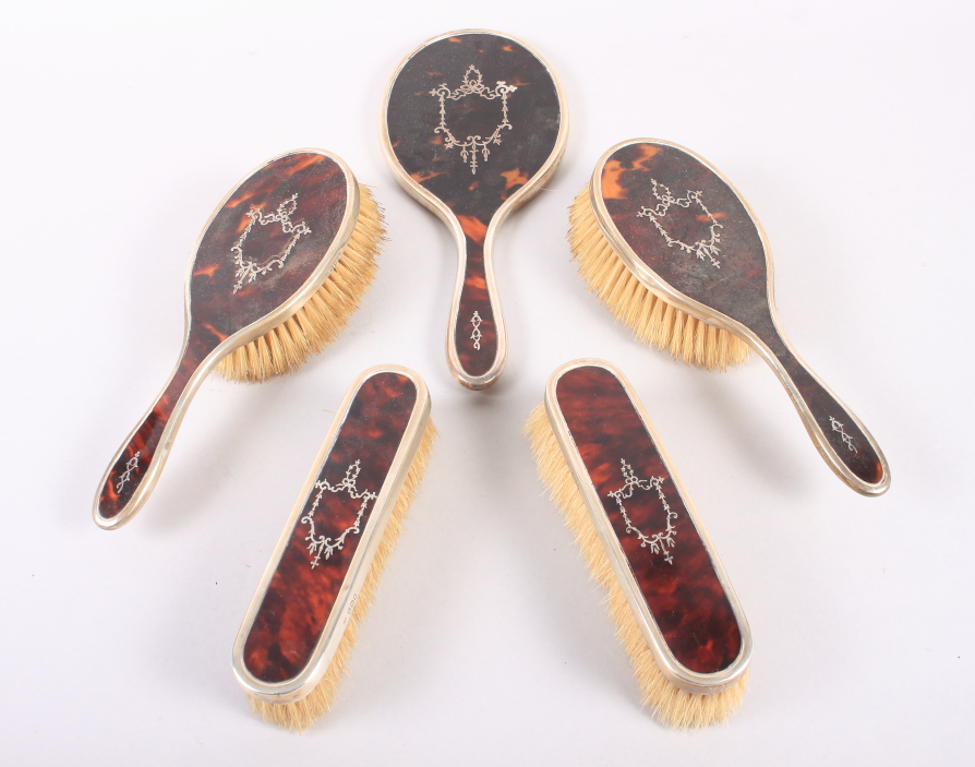 An Edwardian silver and tortoiseshell mounted dressing table set, comprising four brushes and a hand