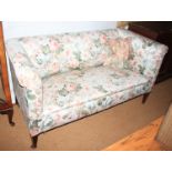 A late 19th century two-seat settee, upholstered in a floral fabric, on square tapering supports,