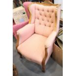 A walnut framed wing back armchair with button back, upholstered in a pink leaf pattern fabric, on