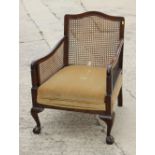 A 1930s bergere armchair with carved mahogany frame, on claw and ball supports