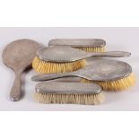 An engraved silver backed dressing table set, comprising four brushes and a hand mirror